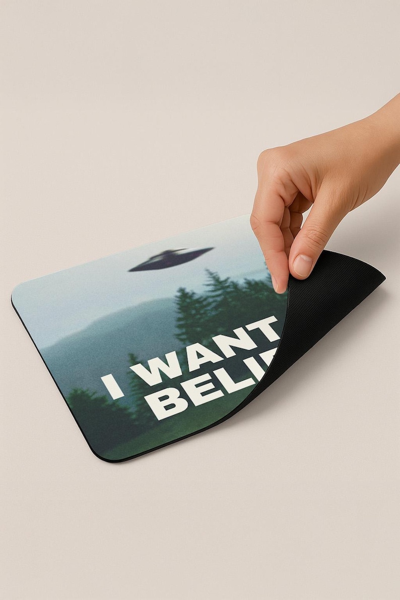 May include: A black and white mousepad with a green, blue, and white image of a flying saucer over a forest. The text "I WANT TO BELIEVE" is printed on the mousepad.