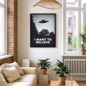 May include: A living room interior with a beige sofa, a wooden coffee table, and two potted plants. A framed poster with the text "I WANT TO BELIEVE" and a flying saucer is hanging on the wall. A woven pendant light hangs from the ceiling.
