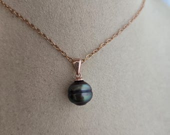 Può includere: Una collana in oro rosa con un pendente di perla verde scuro. Il pendente ha un design a coste unico. La catena è delicata e la chiusura non è visibile. La collana è esposta su una superficie di colore neutro.