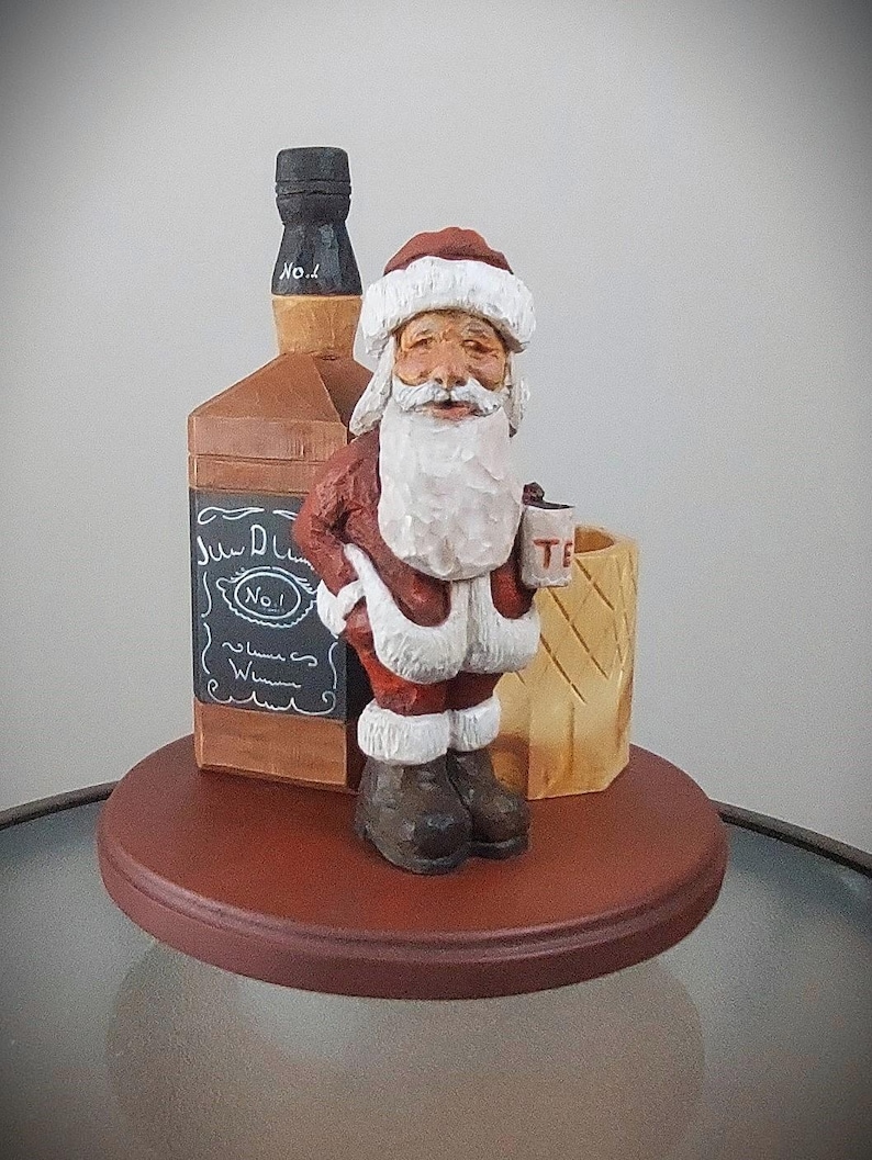 Puede incluir: Una figurita de madera de Pap&aacute; Noel sosteniendo una taza peque&ntilde;a, de pie junto a una botella de whisky y un barril de madera. La botella tiene una etiqueta que dice "Jack Daniel's No. 1 Whiskey".