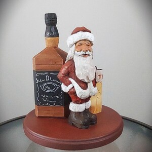 Puede incluir: Una figurita de madera de Pap&aacute; Noel sosteniendo una botella de whisky Jack Daniel's. La figurita est&aacute; de pie sobre una base de madera.
