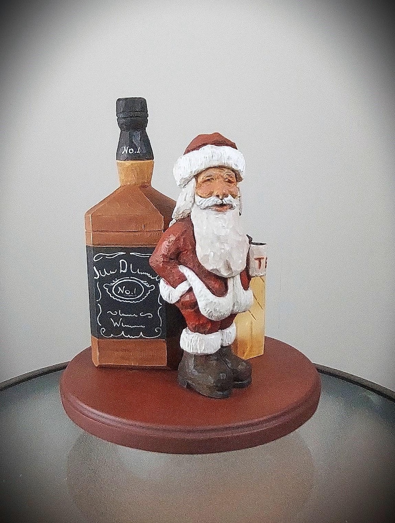 Puede incluir: Una figurita de madera de Pap&aacute; Noel sosteniendo una botella de whisky Jack Daniel's. La figurita est&aacute; de pie sobre una base de madera.