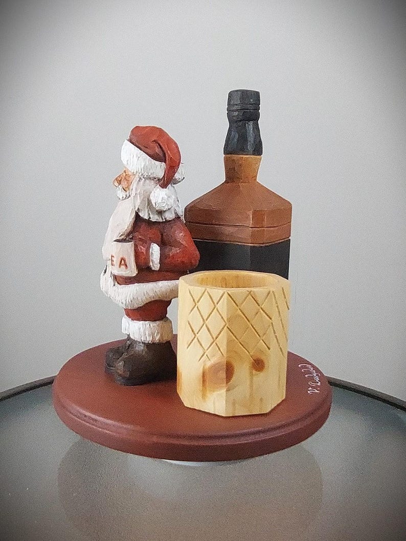 Puede incluir: Una figura de madera de Pap&aacute; Noel sosteniendo una taza, de pie junto a una botella de madera y una taza de madera. La figura est&aacute; pintada de rojo y blanco, y la botella y la taza est&aacute;n pintadas de marr&oacute;n.