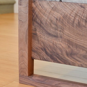 Puede incluir: Primer plano de una cabecera de cama de madera marr&oacute;n oscuro con un dise&ntilde;o simple y moderno. El marco tiene una forma rectangular con un borde elevado y un acabado liso.