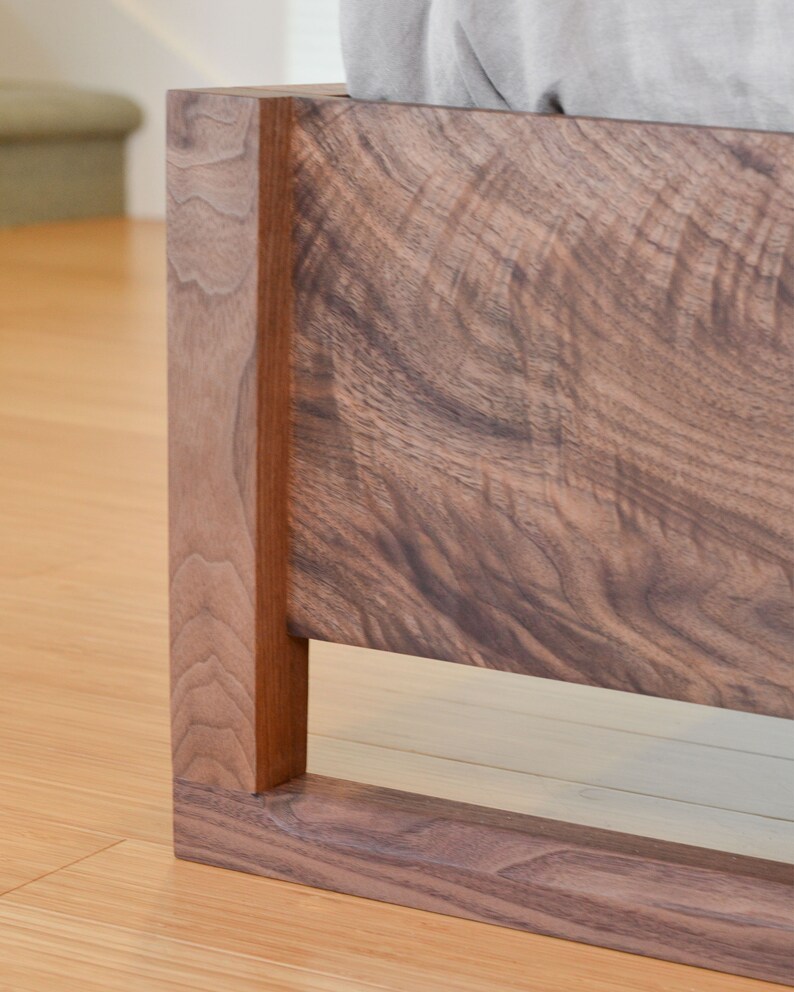 Puede incluir: Primer plano de una cabecera de cama de madera marr&oacute;n oscuro con un dise&ntilde;o simple y moderno. El marco tiene una forma rectangular con un borde elevado y un acabado liso.