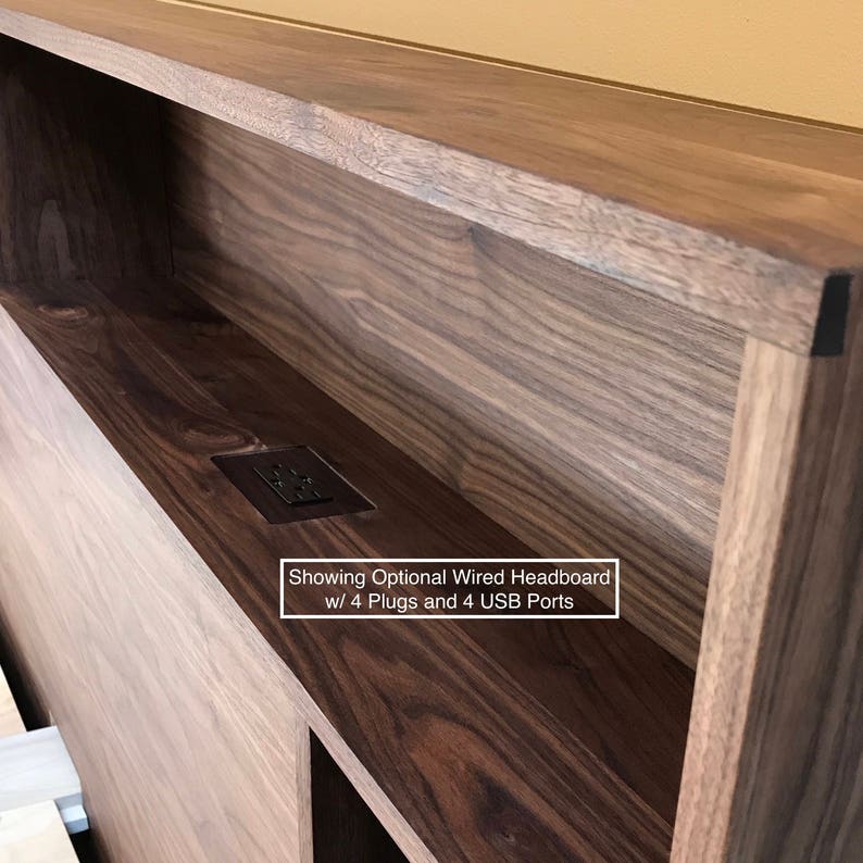 May include: A close-up of a wooden headboard with a built-in electrical outlet. The outlet has four plugs and four USB ports. The text "Showing Optional Wired Headboard w/ 4 Plugs and 4 USB Ports" is visible below the outlet.