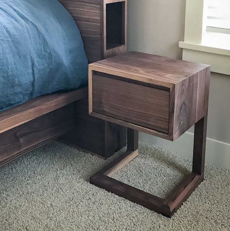 May include: A dark brown wooden nightstand with a single drawer and a square base. The nightstand is made of walnut wood and has a modern design.