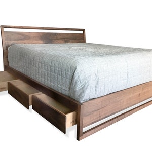 Puede incluir: Un marco de cama de madera con cabecera y piecero. El marco de la cama tiene tres cajones que est&aacute;n parcialmente abiertos. El marco de la cama est&aacute; hecho de madera oscura y tiene un dise&ntilde;o moderno.