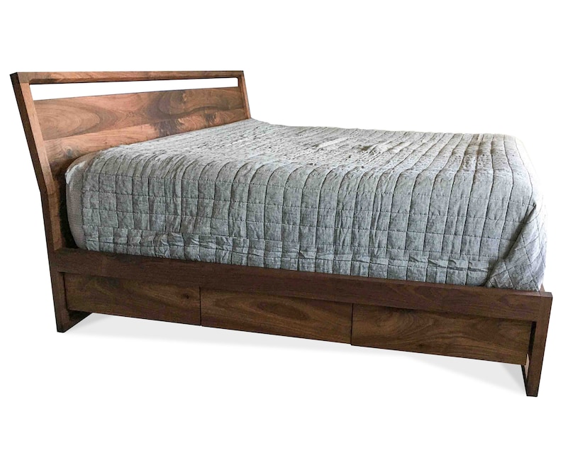 Puede incluir: Un marco de cama de madera con una cabecera de listones y un edred&oacute;n acolchado gris. El marco de cama tiene un caj&oacute;n de almacenamiento debajo.