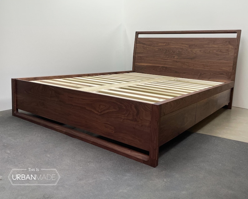 Puede incluir: Un marco de cama plataforma de madera oscura con una cabecera de listones y un caj&oacute;n de almacenamiento debajo. El marco de la cama est&aacute; hecho de madera maciza y tiene un acabado natural.