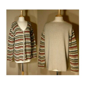 May include: A beige cardigan with brown, white, and pink stripes. The cardigan has a V-neck and button closure. The sleeves are crocheted with the same striped pattern.