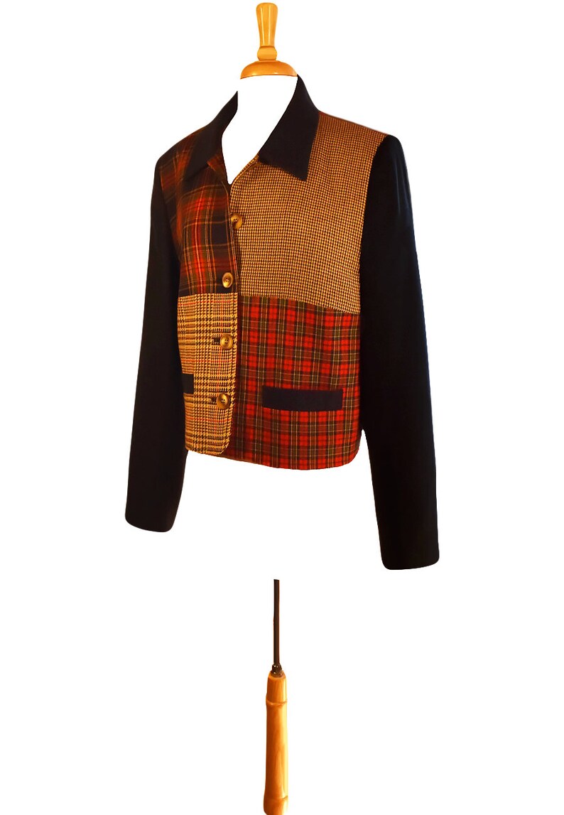 May include: A black, cropped jacket with a patchwork design. The jacket features four different plaid patterns in shades of red, brown, and yellow.
