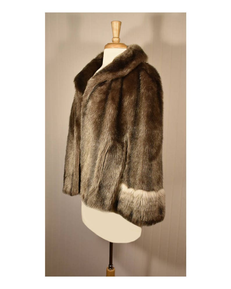 Peut inclure: Une veste en fausse fourrure marron avec un col et des poignets bord&eacute;s de fausse fourrure blanche. La veste est sur un mannequin blanc.