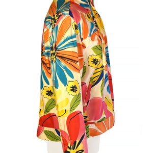 May include: A white, cropped jacket with a colorful floral print. The print features large, abstract flowers in shades of orange, pink, blue, yellow, and green.