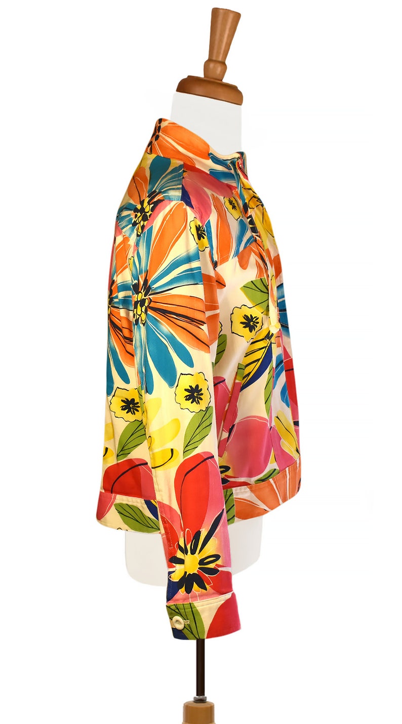 May include: A white, cropped jacket with a colorful floral print. The print features large, abstract flowers in shades of orange, pink, blue, yellow, and green.