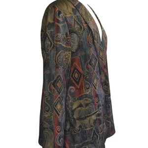 May include: A patterned blazer in shades of green, burgundy, and black. The blazer features a geometric design with diamond shapes and floral accents. It has a notched collar and two front pockets. The blazer is displayed on a mannequin.