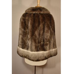 Peut inclure: Une cape en fausse fourrure marron avec une bordure blanche autour du bas. La cape est expos&eacute;e sur un mannequin.