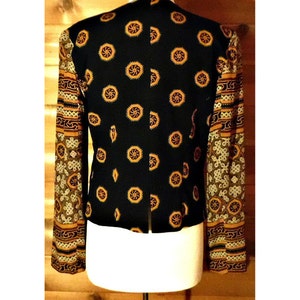 May include: A black blazer with a geometric pattern on the sleeves. The sleeves are made of a sheer fabric with a gold and brown pattern. The blazer is on a white mannequin.