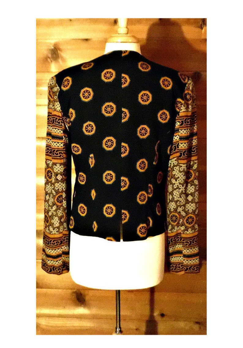 May include: A black blazer with a geometric pattern on the sleeves. The sleeves are made of a sheer fabric with a gold and brown pattern. The blazer is on a white mannequin.