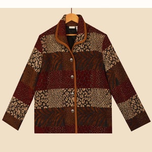 May include: A patchwork jacket with a mix of animal print patterns in shades of brown, tan, and burgundy. The jacket has a brown collar and trim, with silver buttons down the front. The jacket is hanging on a wooden hanger.