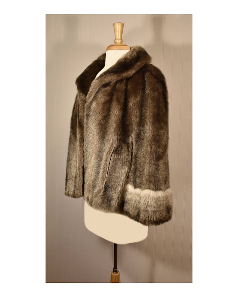Peut inclure: Une veste en fausse fourrure marron avec un col et des poignets bord&eacute;s de fausse fourrure blanche.