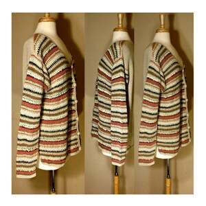 May include: A striped cardigan with a crocheted texture in shades of beige, brown, black, and coral. The cardigan has a button closure and long sleeves.