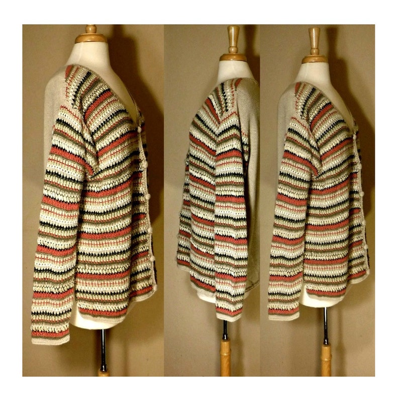 May include: A striped cardigan with a crocheted texture in shades of beige, brown, black, and coral. The cardigan has a button closure and long sleeves.
