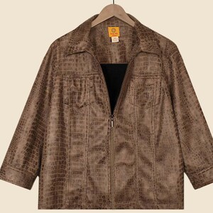 May include: A brown faux-leather jacket with a crocodile skin texture. The jacket has a collared neckline, a zipper closure, and two front pockets. The sleeves are three-quarter length. The jacket is hanging on a wooden hanger.