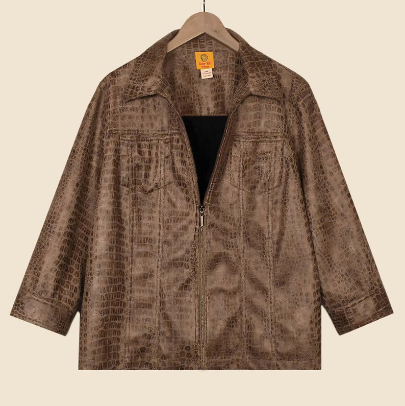 May include: A brown faux-leather jacket with a crocodile skin texture. The jacket features a collared neckline, two chest pockets, and a full-length zip. The sleeves are three-quarter length. The jacket hangs on a wooden hanger.