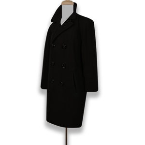 K&ouml;nnte beinhalten: Ein schwarzer Peacoat mit doppelreihigem Verschluss und vier schwarzen Kn&ouml;pfen. Der Mantel hat zwei Taschen auf der Vorderseite.