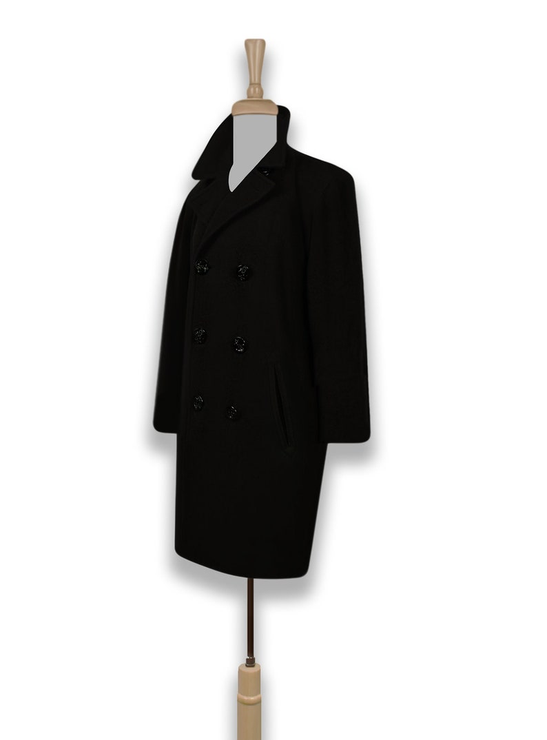 K&ouml;nnte beinhalten: Ein schwarzer Peacoat mit doppelreihigem Verschluss und vier schwarzen Kn&ouml;pfen. Der Mantel hat zwei Taschen auf der Vorderseite.