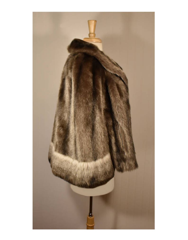 Peut inclure: Une veste en fausse fourrure marron avec une bordure en fourrure blanche autour du bas et des manches. La veste est sur un mannequin blanc.