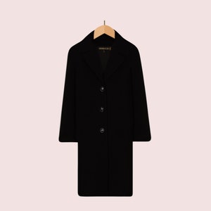 May include: A black long-sleeved coat with a collar and button fastening. The coat is hanging on a wooden hanger.