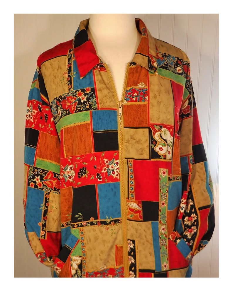 May include: A long-sleeved jacket with a zipper closure. The jacket is made of a patchwork fabric with a variety of colors and patterns, including red, blue, green, and brown. The fabric has a floral design.