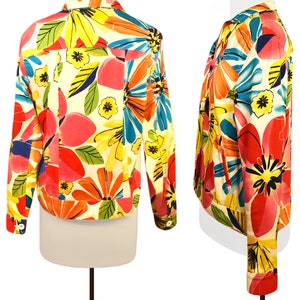 May include: A white denim jacket with a colorful floral print. The print features large flowers in shades of pink, orange, yellow, blue, and green.