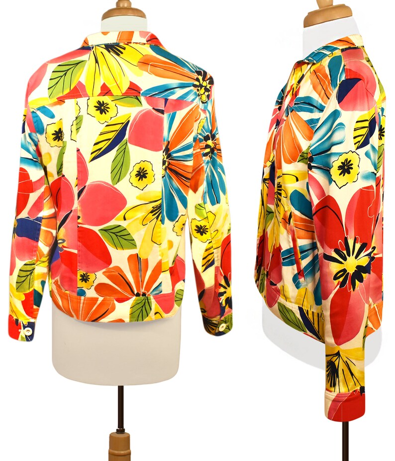 May include: A white denim jacket with a colorful floral print. The print features large flowers in shades of pink, orange, yellow, blue, and green.