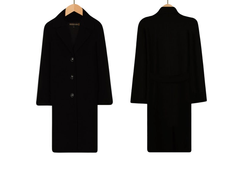 May include: A black long-sleeved coat with a collar and three buttons down the front. The coat has a belt at the waist and is hanging on a wooden hanger.