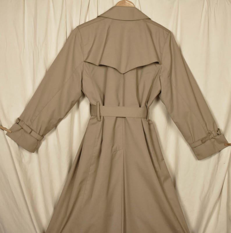 K&ouml;nnte beinhalten: Ein beiger Trenchcoat mit G&uuml;rtel und doppelreihigem Verschluss. Der Mantel hat ein klassisches Design und ist aus leichtem Stoff gefertigt.