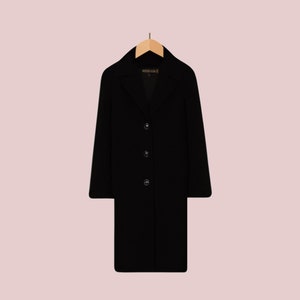May include: A black long-sleeved coat with a collar and button closure. The coat is hanging on a wooden hanger.