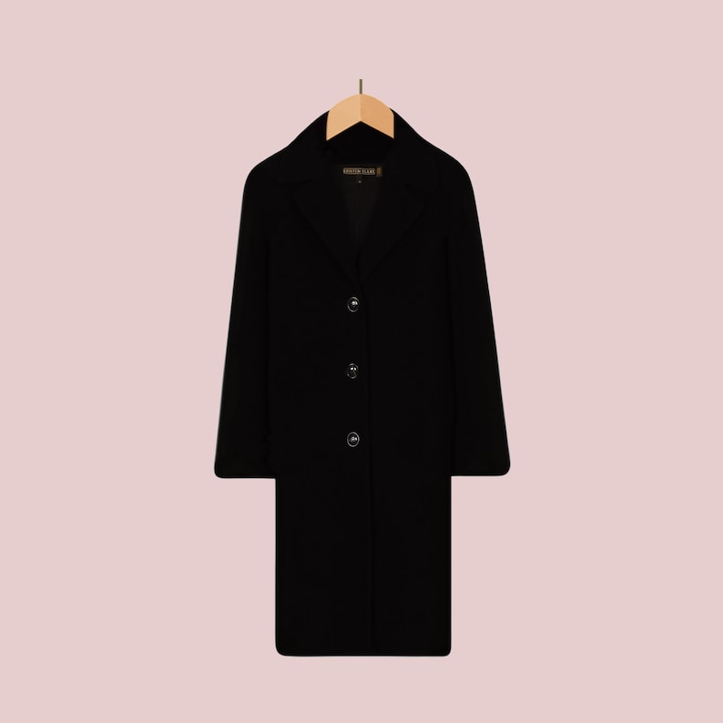May include: A black long-sleeved coat with a collar and button closure. The coat is hanging on a wooden hanger.