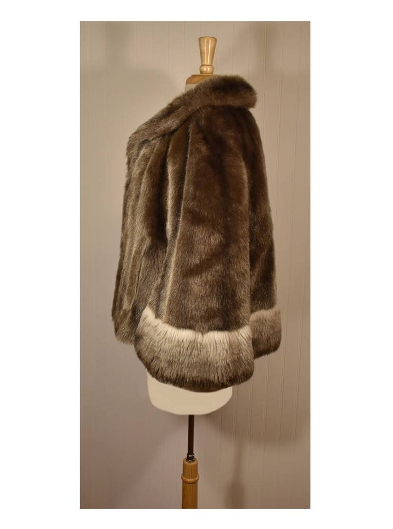 Peut inclure: Une veste en fausse fourrure marron avec une bordure blanche autour des bords. La veste est sur un mannequin blanc.