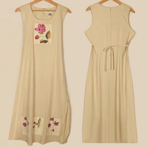 May include: A sleeveless, beige linen dress with a floral print. The dress has a tie at the back and a slit on the side.
