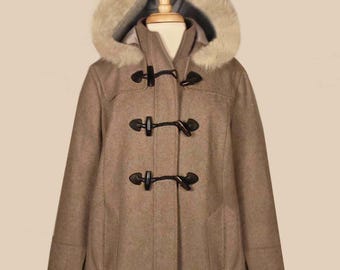 Puede incluir: Un abrigo tipo duffel de color beige con capucha forrada de piel sintética. El abrigo tiene tres cierres de palanca y dos bolsillos delanteros. El abrigo se exhibe en un maniquí.