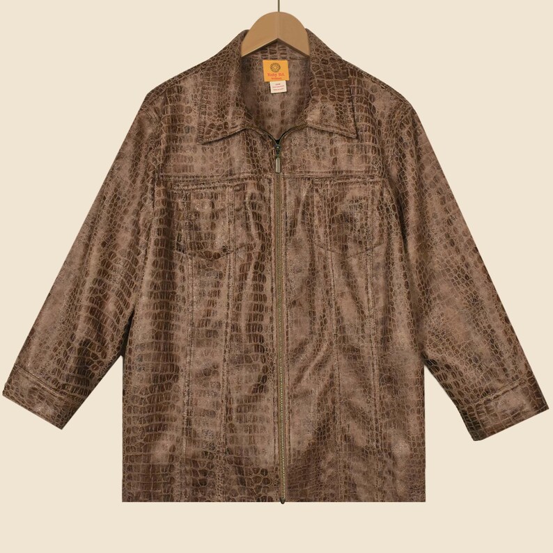 May include: Brown faux-leather jacket with a crocodile skin texture. The jacket features a collared neckline, a zip closure, and two chest pockets. The jacket is hanging on a wooden hanger.