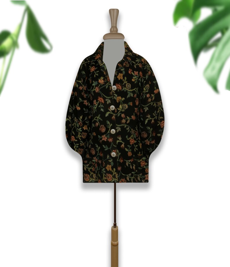May include: A black button-up shirt with a floral pattern in shades of orange, green, and brown. The shirt is on a mannequin.