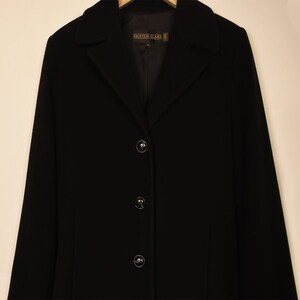 May include: A black long-sleeved coat with a collar and four buttons. The label on the coat reads "Kristen Blake".