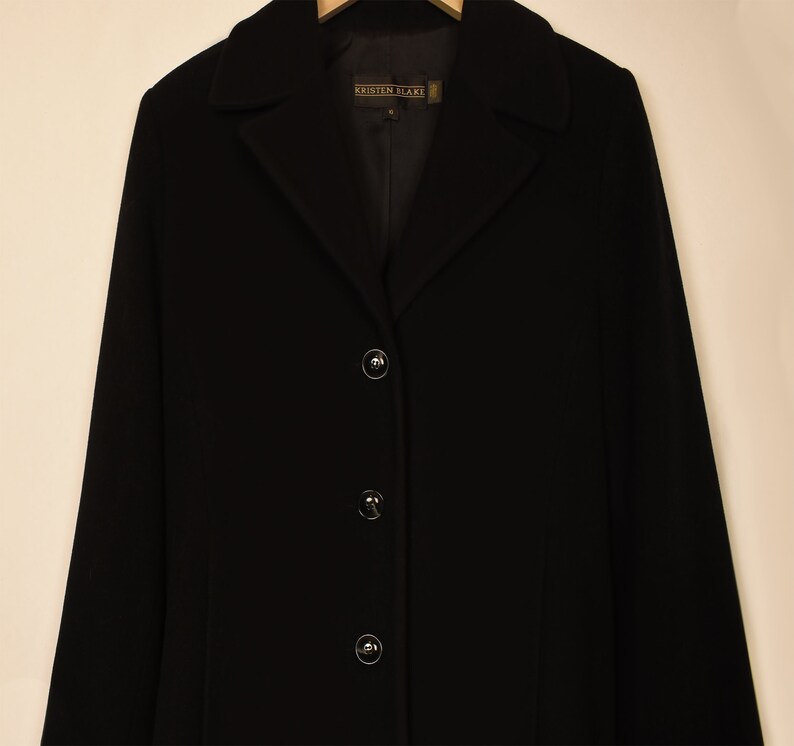 May include: A black long-sleeved coat with a collar and four buttons. The label on the coat reads "Kristen Blake".
