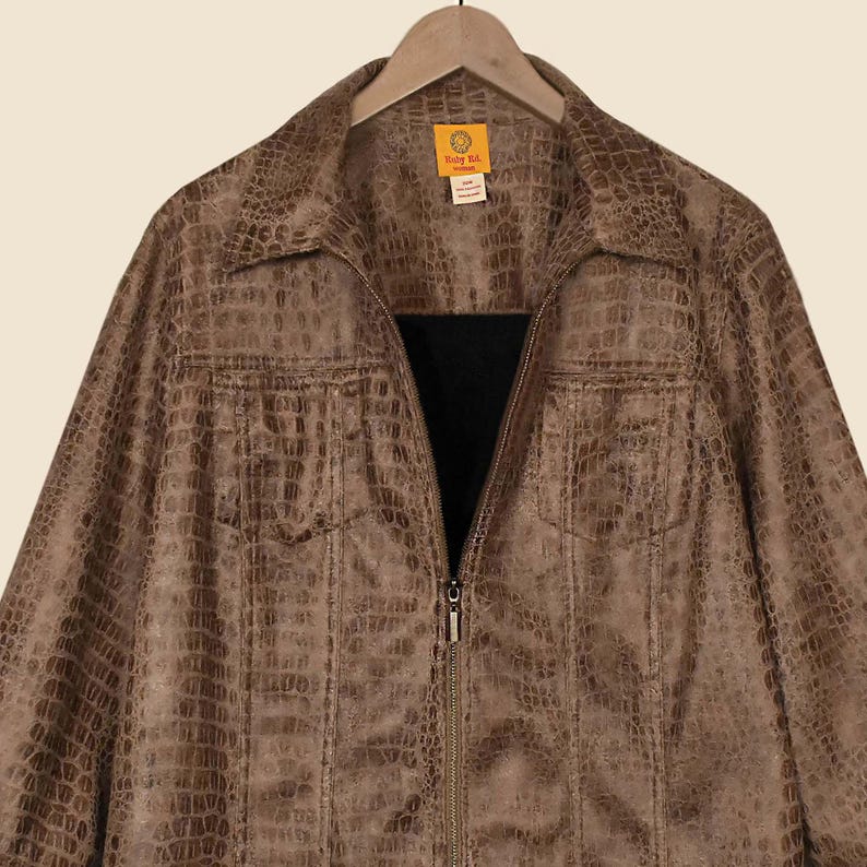 May include: A brown faux leather jacket with a reptile skin texture, featuring a collared neckline and a full-length zip. The jacket has two front pockets and is hanging on a wooden hanger.