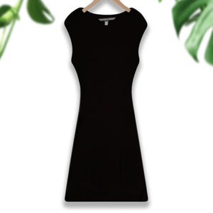 May include: A black sleeveless dress with a scoop neck and a fitted silhouette. The dress has a small tag that says "Victoria's Secret" on the front.