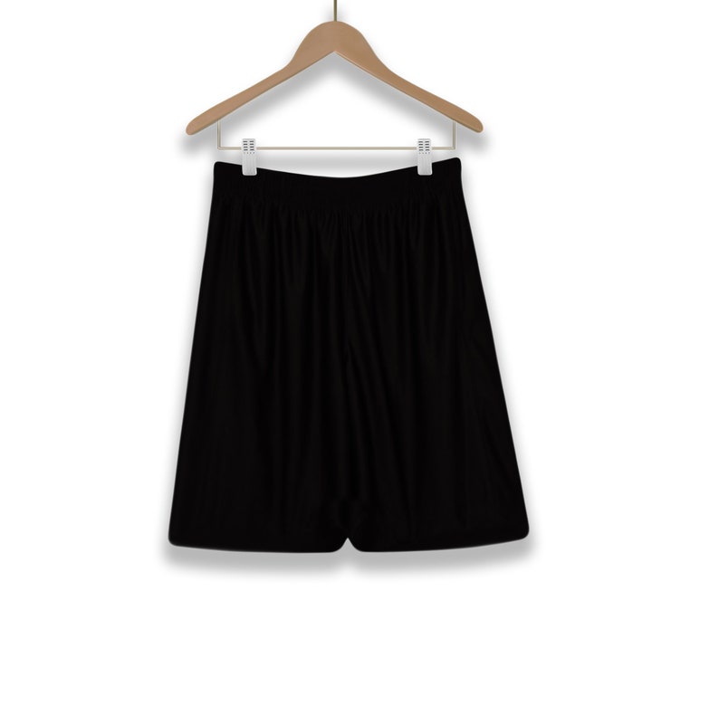 Puede incluir: Pantalones cortos deportivos negros colgados de una percha de madera. Los pantalones cortos tienen un dise&ntilde;o sencillo y una textura lisa.